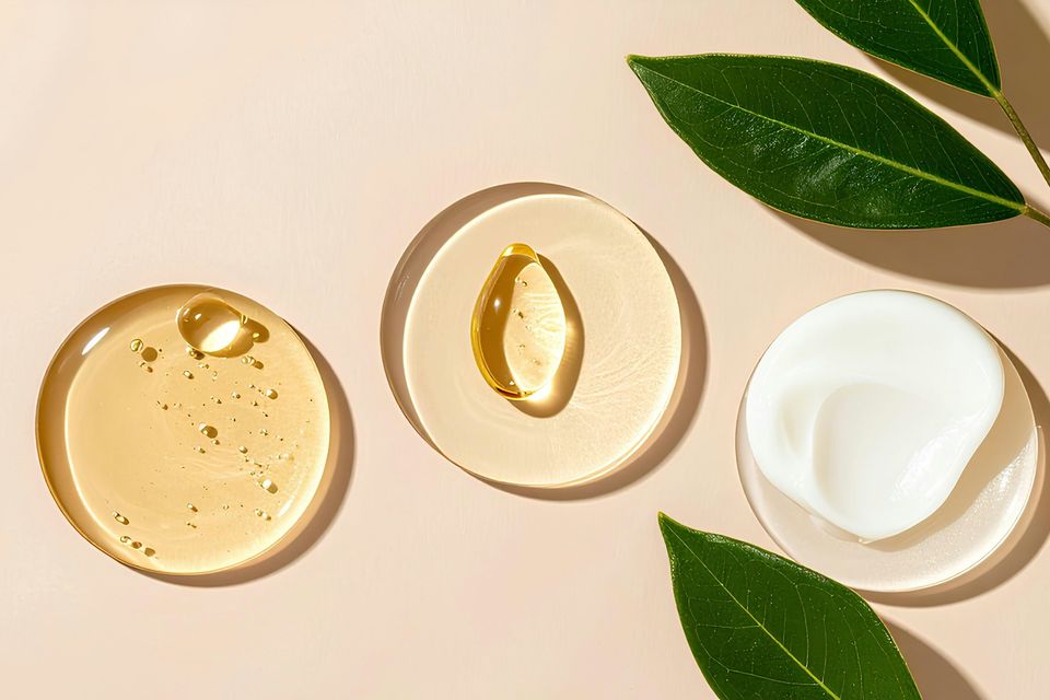 Gotas de gel transparente, óleo e creme em discos de vidro sobre fundo pêssego com folhas verdes