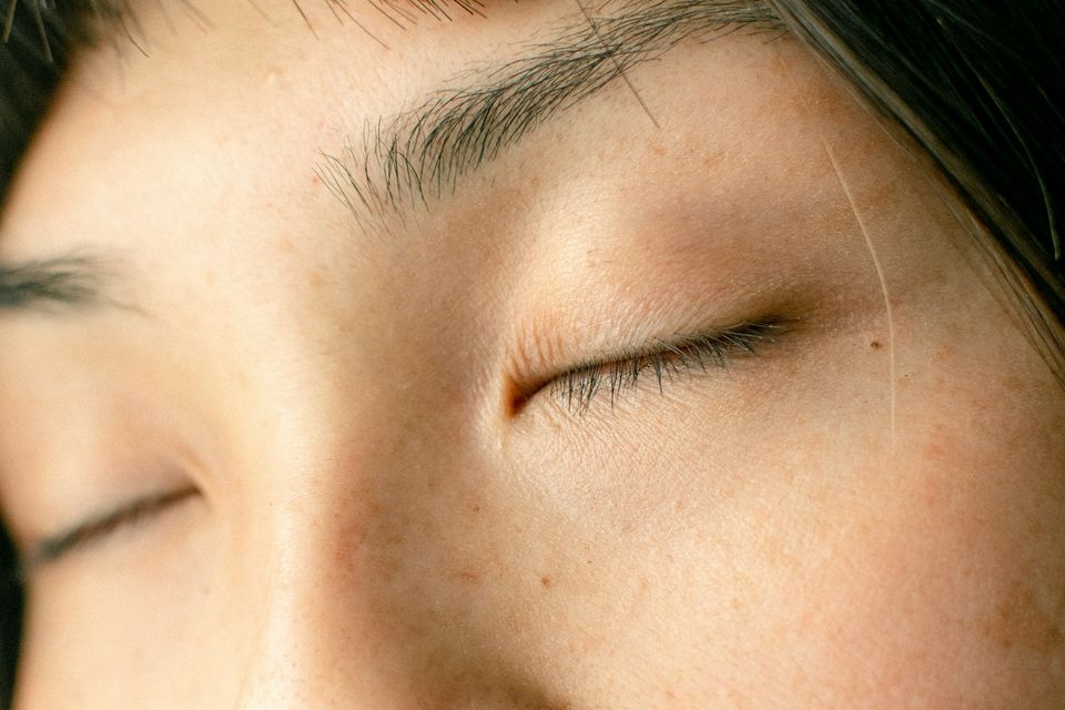 Close do rosto de uma mulher de olhos fechados, com pele natural e leves sardas