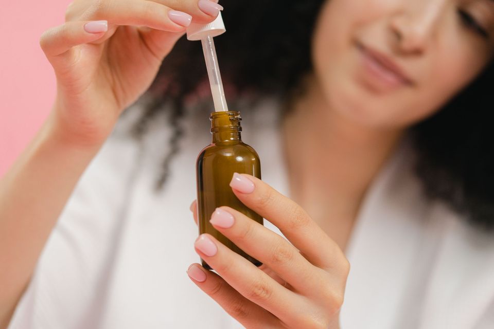 Mulher segurando um frasco âmbar sem rótulo e retirando o conta-gotas de sérum