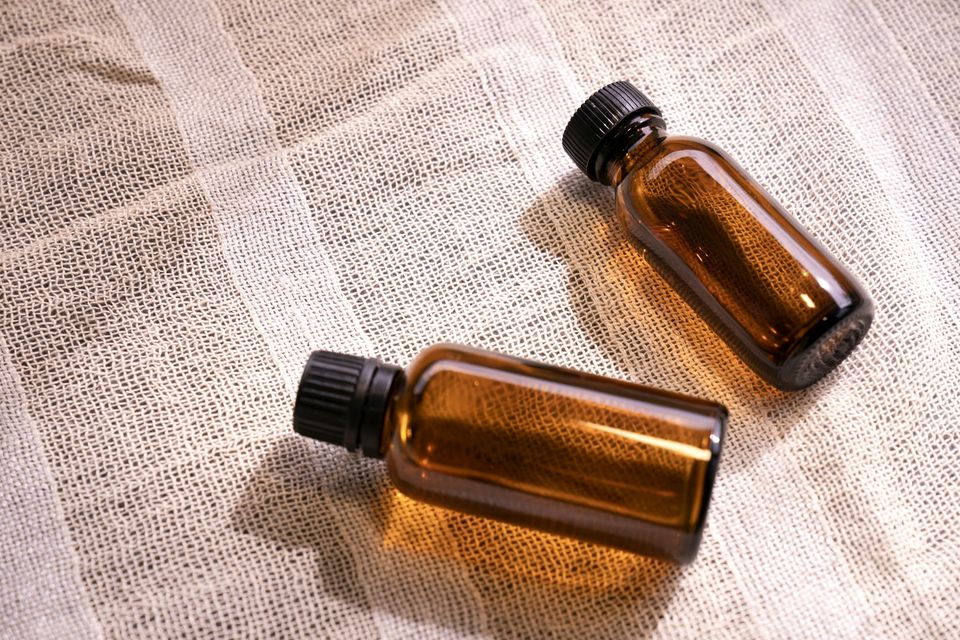 Dois frascos pequenos de vidro âmbar com tampa preta sobre um tecido de gaze claro