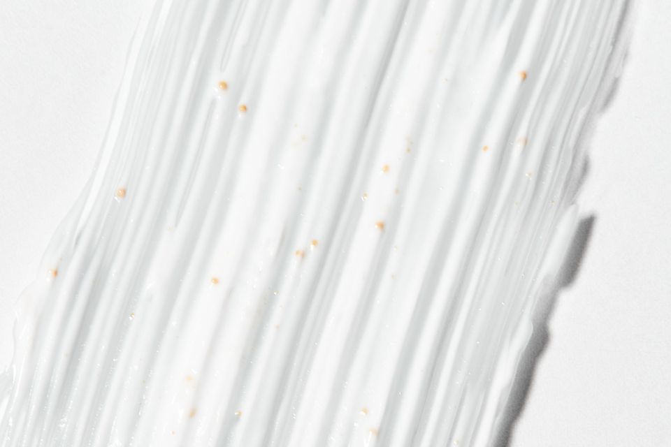 Textura de creme hidratante branco com pequenas partículas bege espalhado sobre fundo claro