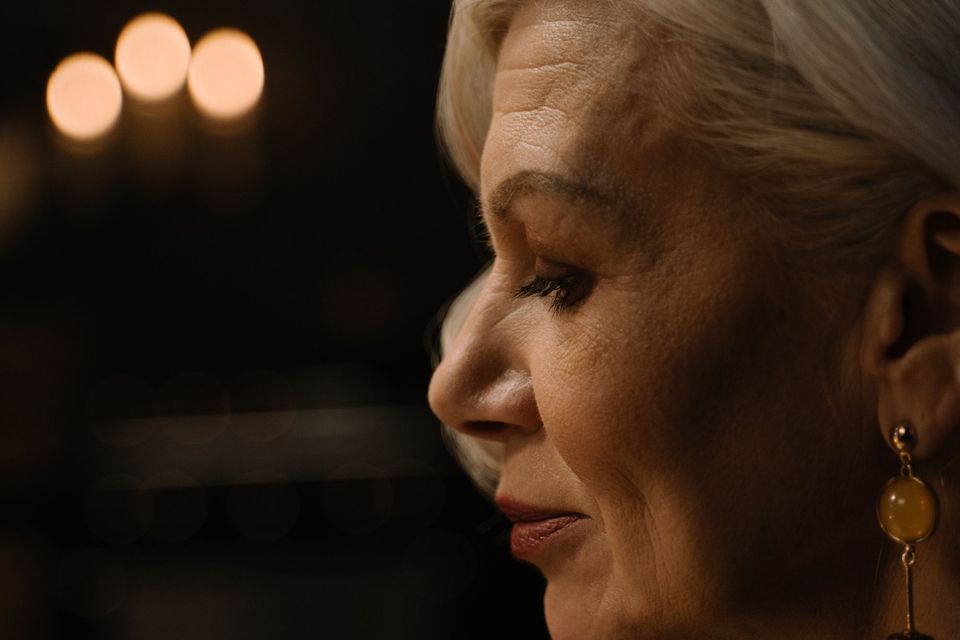 Perfil do rosto de uma mulher madura de cabelo claro, em luz suave e fundo escuro
