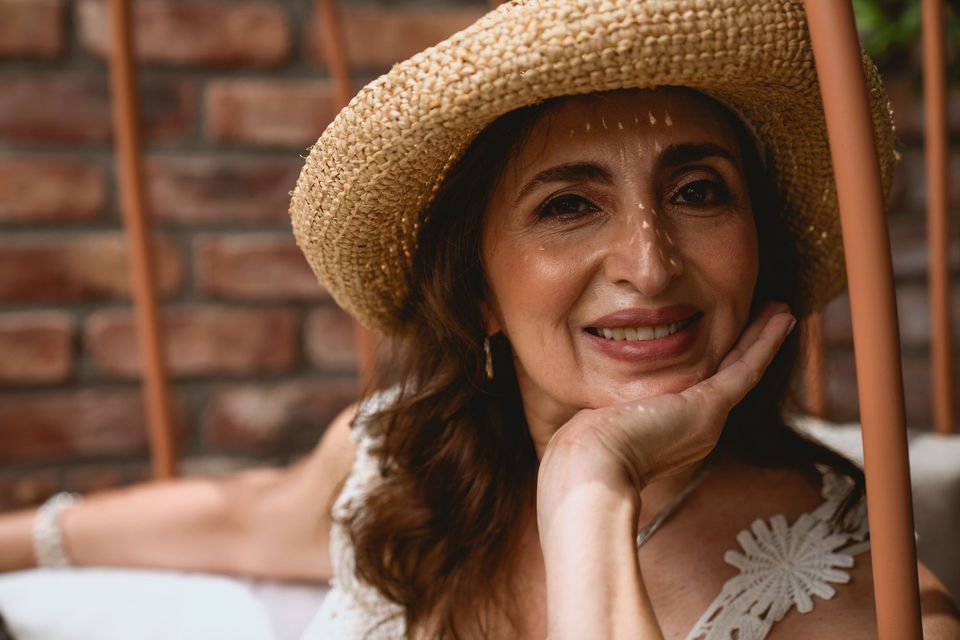 Mulher madura sorrindo com chapéu de palha, com sombra de luz do sol no rosto