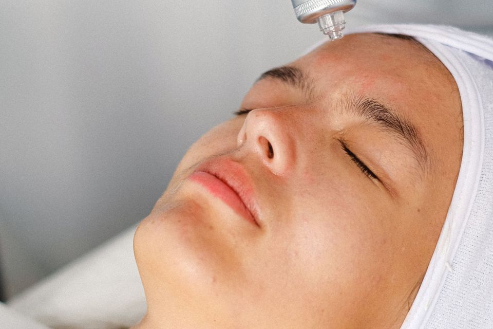 Mulher deitada recebendo tratamento facial com aparelho em consultório claro