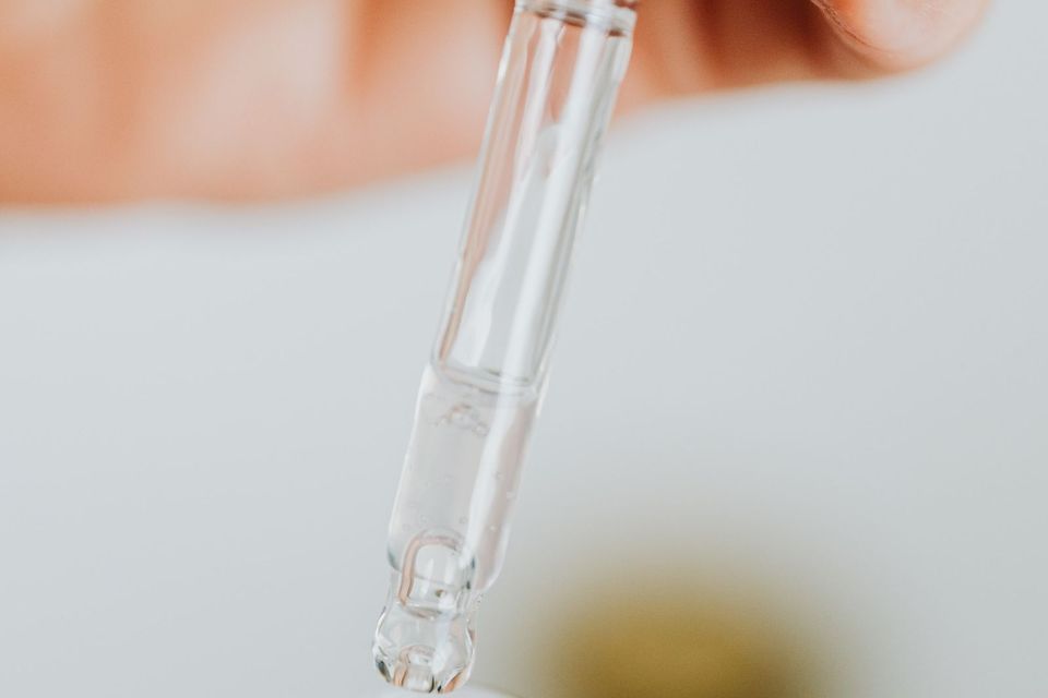Pipeta transparente pingando líquido sobre um frasco de vidro fosco, em close