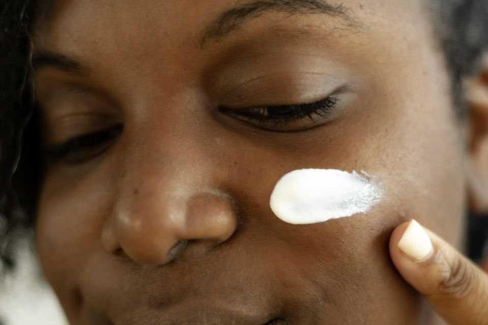 Mulher aplicando creme no rosto, com uma porção sobre a bochecha