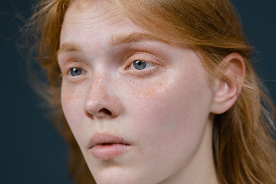 Close do rosto de uma mulher ruiva de pele clara com sardas e leve rubor nas bochechas