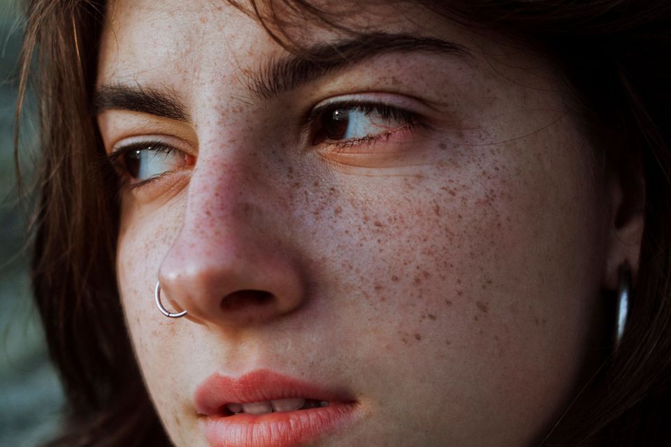 Close do rosto de uma jovem com sardas, em luz natural, olhando para o lado