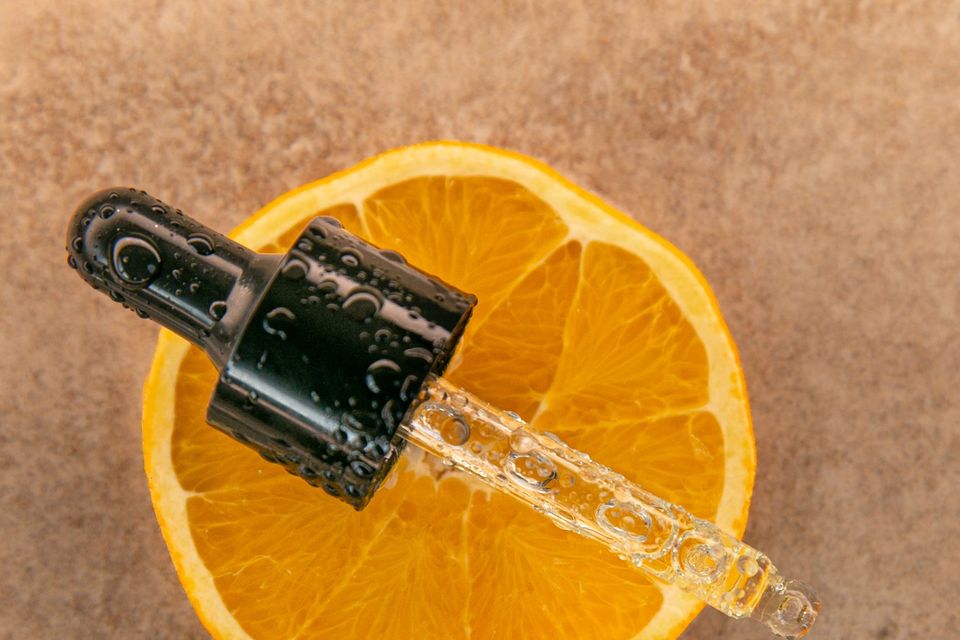 Conta-gotas com gotas de líquido sobre uma metade de laranja, em fundo terroso