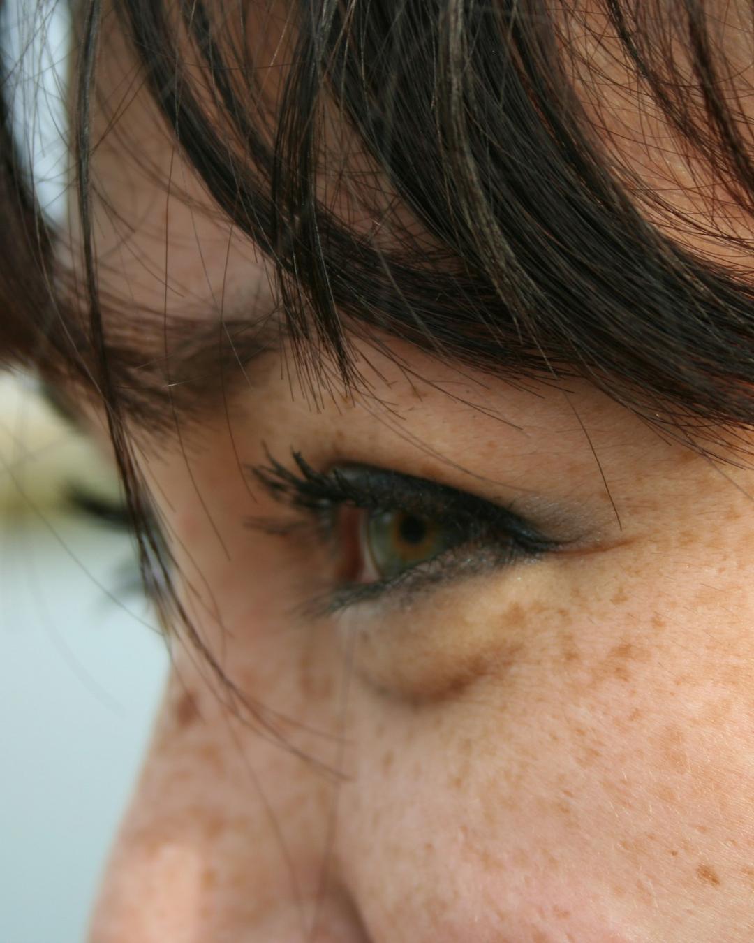 Close do olho e da pele com sardas de uma mulher de cabelo escuro
