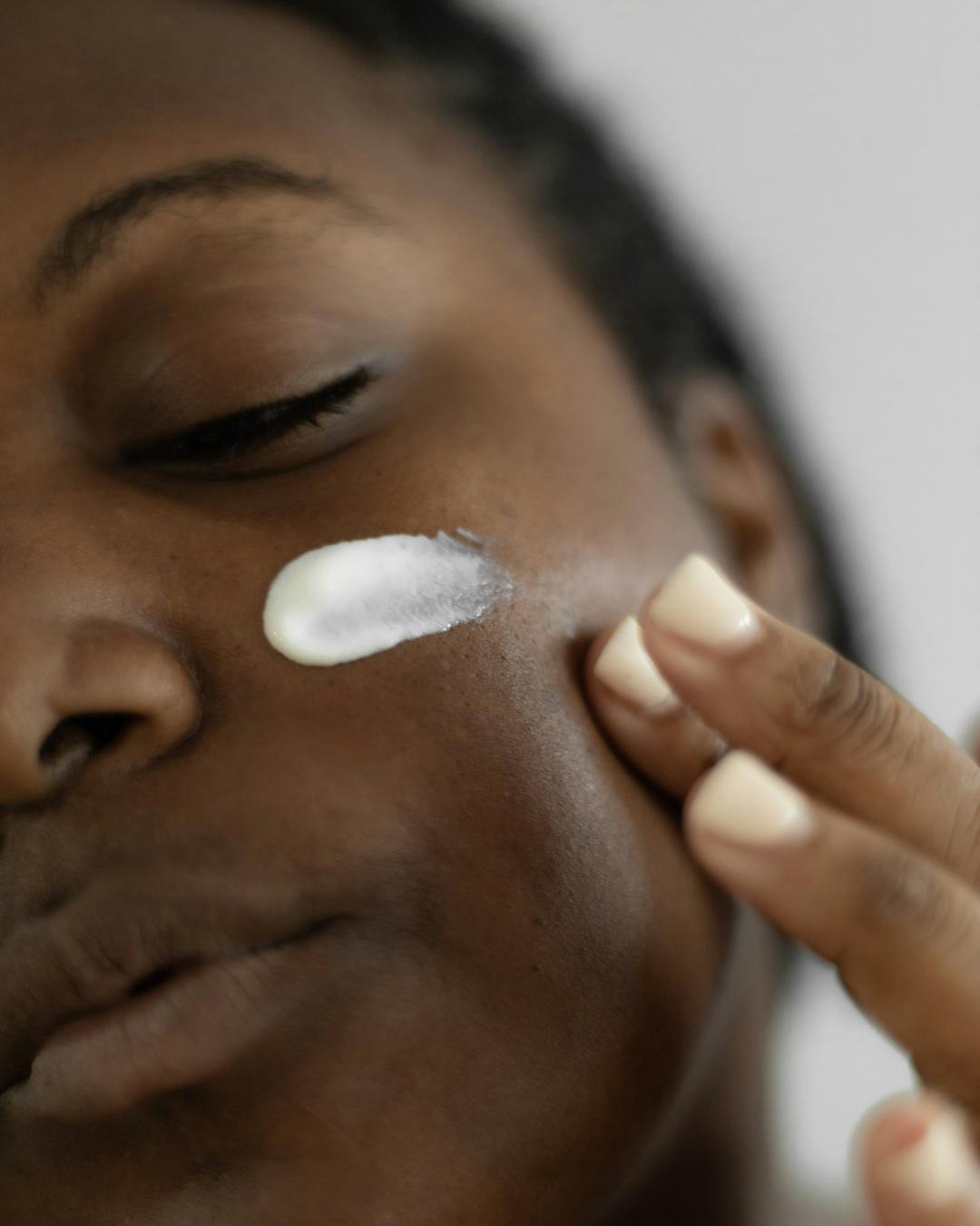 Rosto de mulher com creme aplicado na bochecha, pele real em luz suave